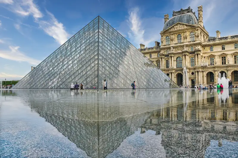 The glass pyramid of the Louvre reflected in still water in Paris