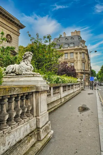A carved stone sphinx on a balustrade beside a Paris street