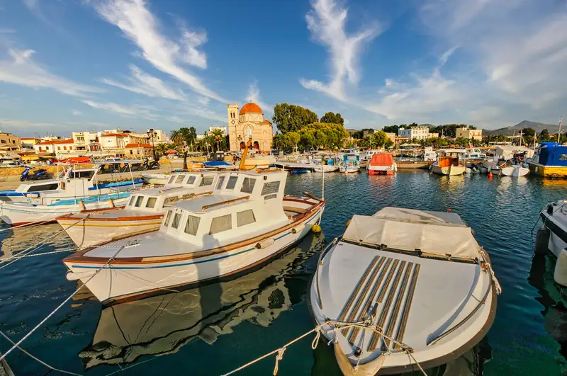 Traditional fishing boats in Aegina Town port with a Byzantine church dome and neoclassical buildings reflected in the calm harbor water
