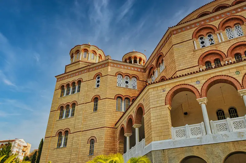 Grand facade of the Agios Nektarios Monastery in Aegina with ornate arched windows and Byzantine architectural details in warm stone