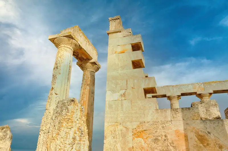 Ancient stone columns and architrave of the Temple of Aphaia in Aegina seen from below against the open sky, showing Doric architectural details