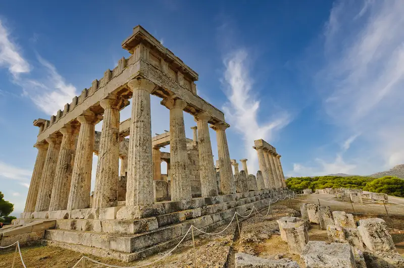 Full view of the Temple of Aphaia in Aegina with its rows of standing Doric columns surrounded by pine trees and the archaeological site