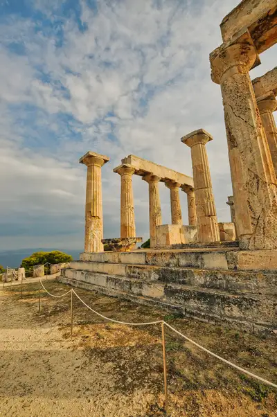 Side view of the Temple of Aphaia in Aegina showing standing columns and stone platform with the Saronic Gulf coastline visible in the distance