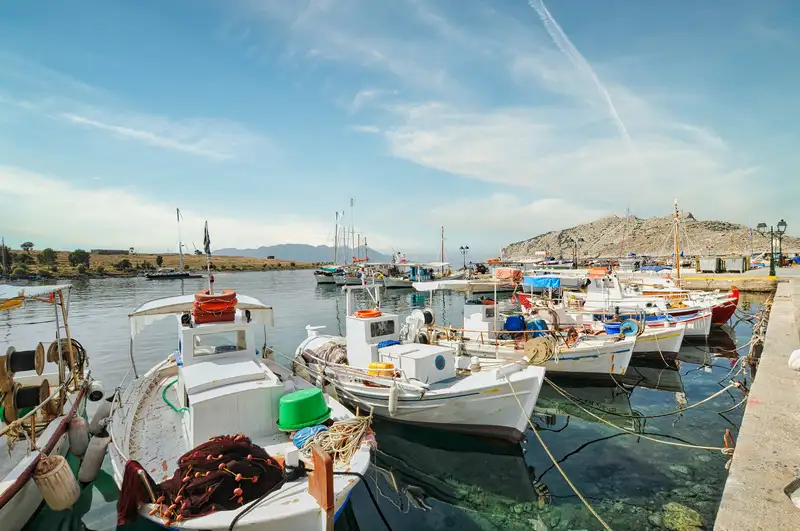 Traditional Greek fishing boats with colorful nets and equipment moored at the small port of Perdika village in Aegina