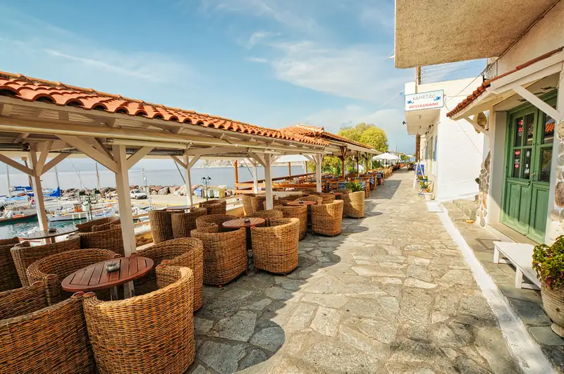 Waterfront taverna terrace in Perdika village Aegina with wicker chairs and tables set along the seafront promenade facing the small harbor
