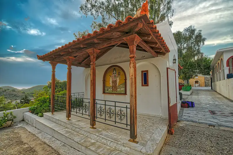 Small open chapel with a wooden canopy and mosaic icon of Saint Nektarios in the monastery grounds of Agios Nektarios in Aegina with hills visible behind