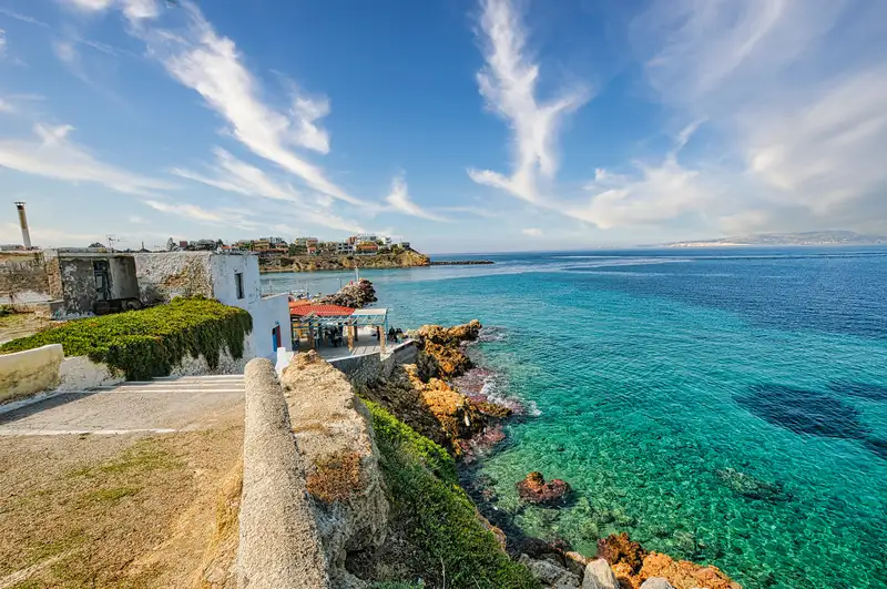 Coastal view of Souvala village in Aegina showing whitewashed buildings along rocky shores with turquoise clear water and the village harbor stretching into the distance