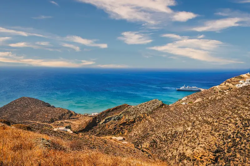 Anafi island coastline view with a ferry arriving at the port and golden hills rolling toward the sea
