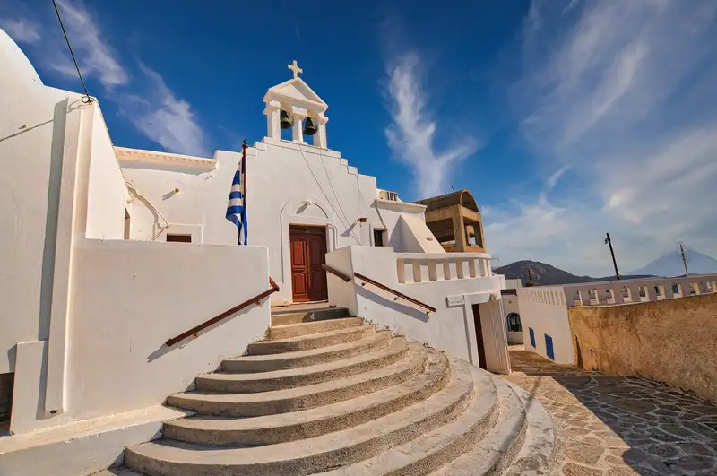 Traditional whitewashed church with bell tower and curved steps in Anafi Chora village