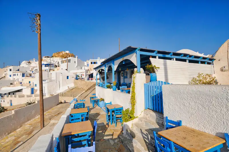 Traditional Anafi taverna in Chora with blue wooden tables and chairs overlooking whitewashed houses