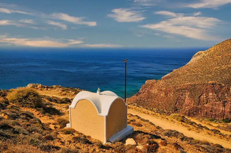 Small whitewashed chapel perched on Anafi's coastline with sea views and golden hills