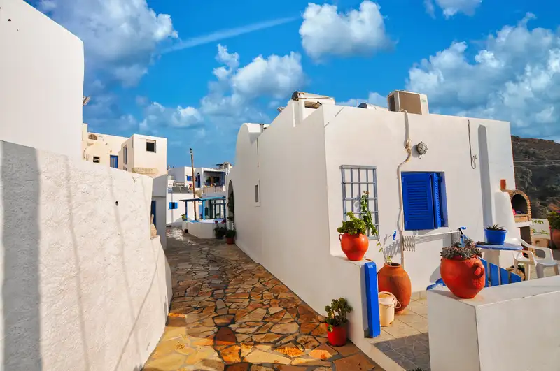 Narrow stone alley in Anafi Chora with blue shutters, whitewashed walls, and terracotta flower pots