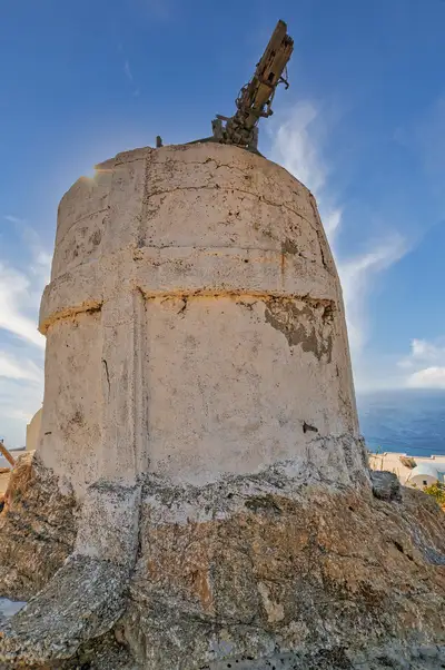 Weathered old windmill in Anafi with worn stone walls and a wooden sail frame against the sky