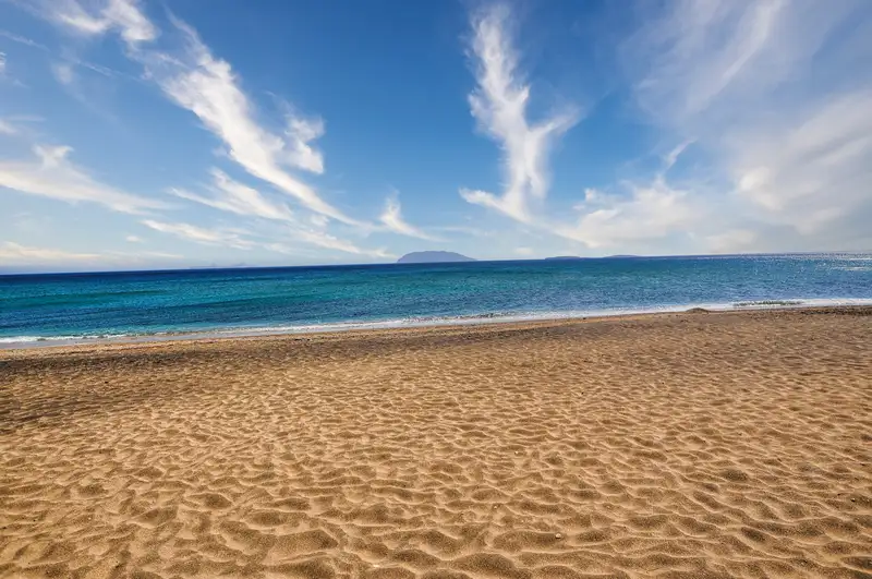 Empty golden sand and deep blue Aegean at Roukounas beach in Anafi, one of the quietest beaches in the Cyclades