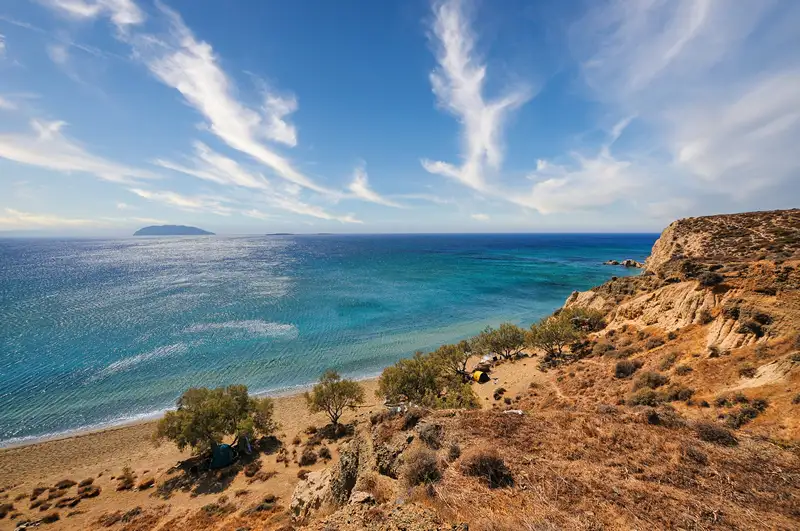 Roukounas beach in Anafi with golden sand, turquoise waters, and olive trees along the shore