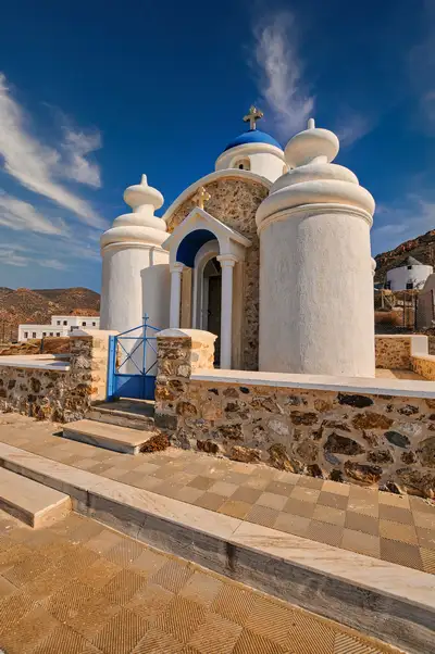 Traditional white chapel in Anafi with blue dome, small cupolas, and a stone courtyard