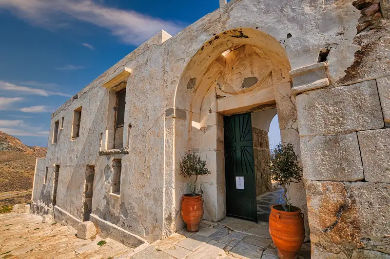 Arched stone entrance of the Zoodochos Pigi Monastery in Anafi with old walls and terracotta pots