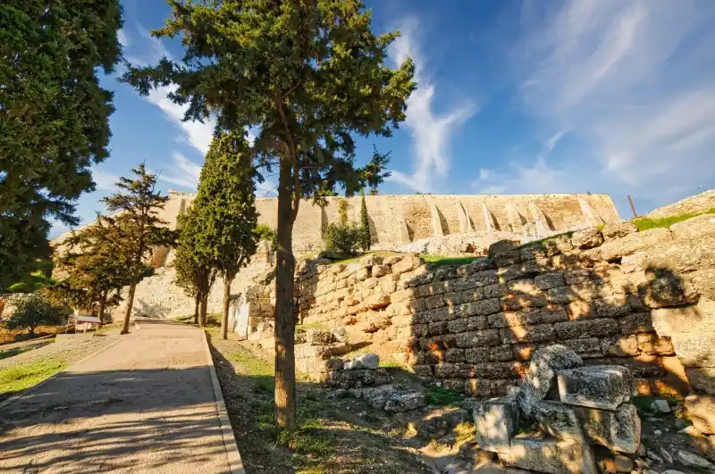 Walking path on the southeastern slope of the Acropolis of Athens with ancient stone walls and trees