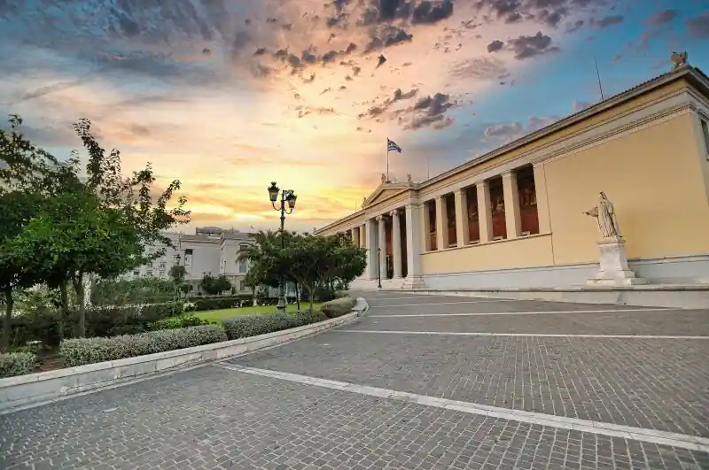 The University of Athens neoclassical building with its long Ionic colonnade, gardens, and a statue near the entrance