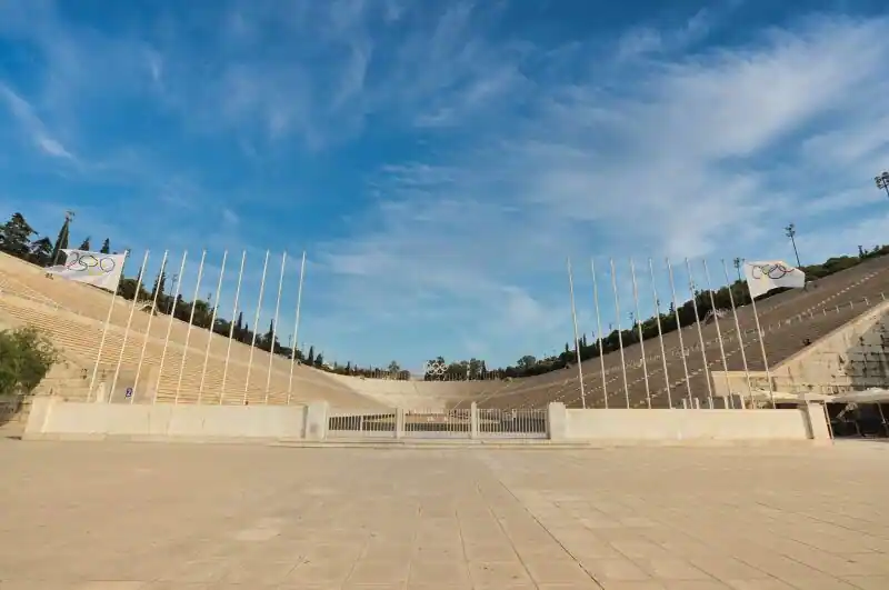 The Panathenaic Stadium in Athens with marble seats and Olympic flags under a blue sky