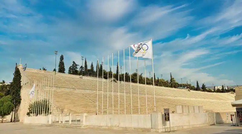 The marble seating of the Panathenaic Stadium in Athens with Olympic and Greek flags flying along the top edge