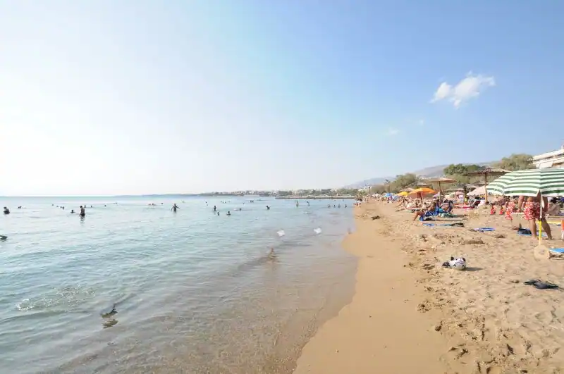 Kavouri beach near Vouliagmeni with swimmers enjoying the calm shallow waters and colorful umbrellas lining the sand