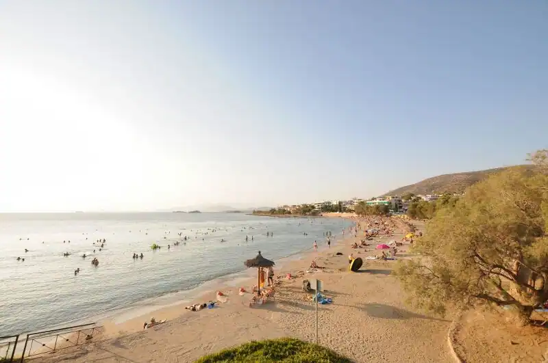 Saronida beach south of Athens with swimmers in the sheltered bay, sandy shore, and hillside town in the background