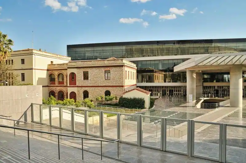 Acropolis Museum exterior with modern glass architecture and historic building in foreground, Athens Greece