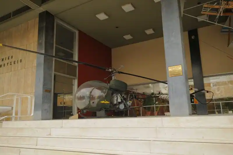 Military helicopter displayed at the entrance of the War Museum in Athens with the Greek sign Πολεμικό Μουσείο visible on the wall