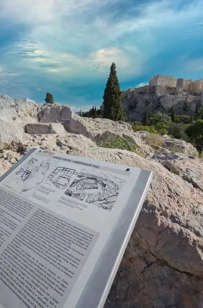 View of the Acropolis from Areopagus Hill in Athens with an information board on the limestone rock in the foreground
