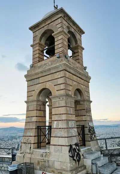 The stone bell tower of Saint George chapel at the top of Lycabettus Hill with Athens spreading out below