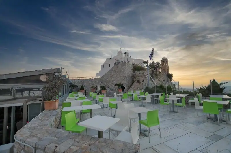The hilltop cafe on Lycabettus Hill with white tables and green chairs and the chapel in the background