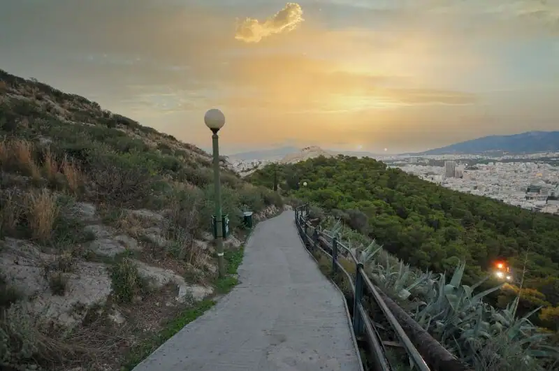 Paved walking path on a hill in Athens with a view of the city and Lycabettus Hill at sunset