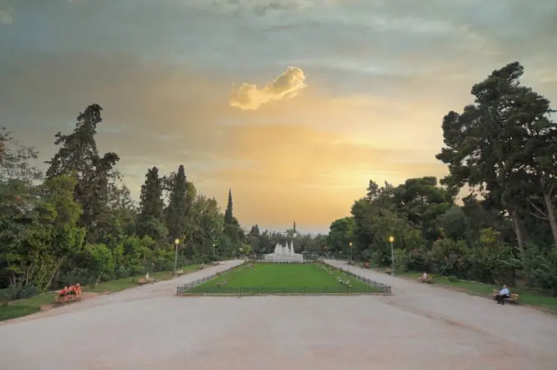 Wide view of the Zappeion Hall gardens at golden hour with pathways, benches, and lush greenery in Athens
