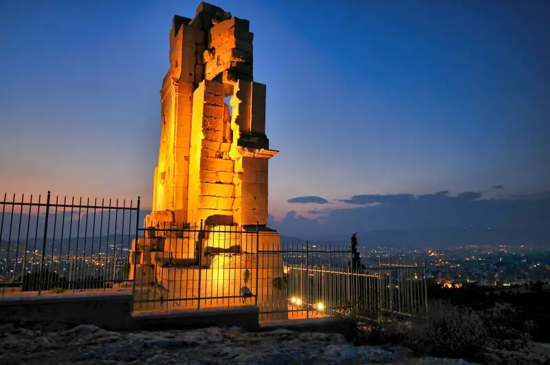 The Philopappos Monument illuminated at night with the lights of Athens spreading out below the hill