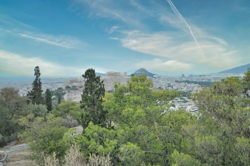 View from Philopappos Hill in Athens showing the Acropolis and Lycabettus Hill through green pine and cypress trees