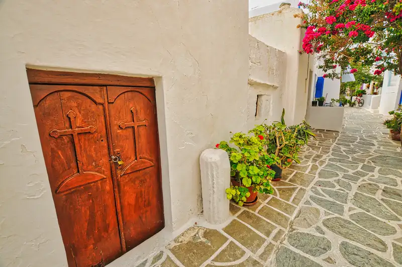 Wooden church door with cross carvings in Kastro Folegandros, with stone-paved alley