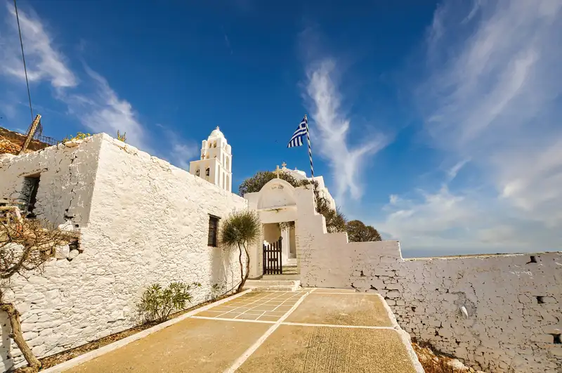 Panagia church path in Folegandros with whitewashed courtyard and Greek flag