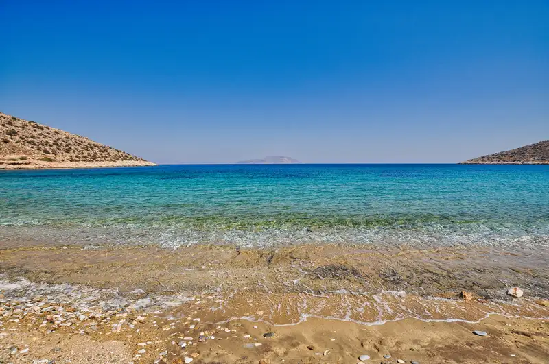 The shallow turquoise water of Agia Theodoti beach in Ios, with a Cycladic island in the distance