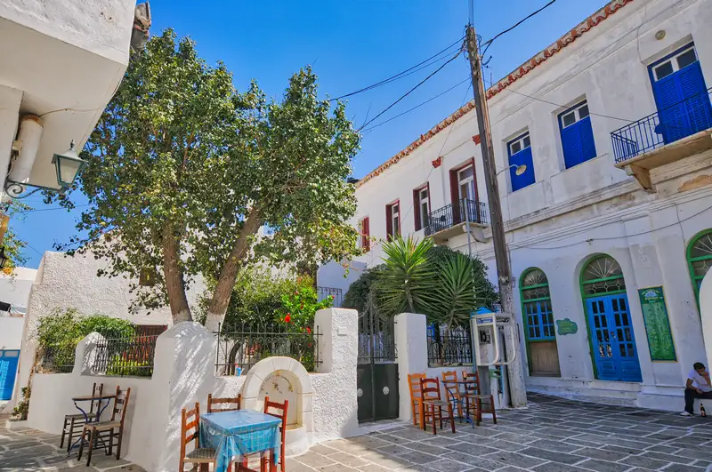 A small square in Chora village of Ios with a tree, traditional houses, and a cafe table