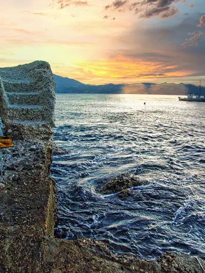 A stone pier and a small fishing boat at sunset in Klima village on Milos island