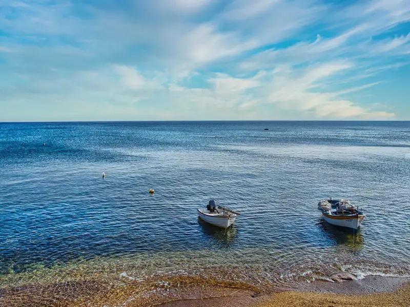 Small fishing boats anchored in the clear waters of Paliochori beach on Milos island