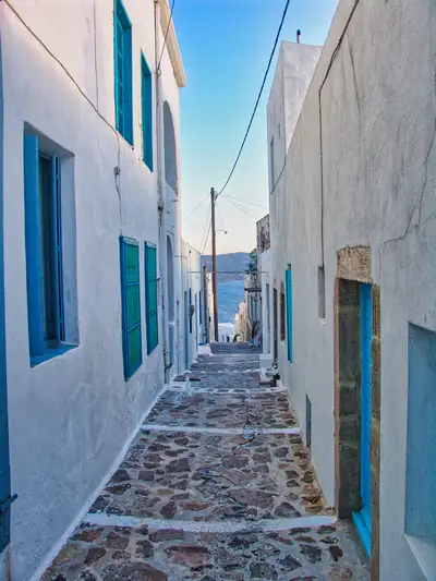 A narrow whitewashed alley with blue shutters and a stone-paved street in Plaka village on Milos island