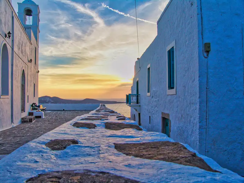 A view from a Plaka terrace at sunset with the bell tower of a Cycladic church and the Aegean Sea on Milos island
