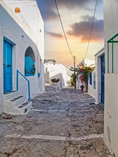 A traditional stone-paved alley in Plaka village with whitewashed houses and red bougainvillea on Milos island