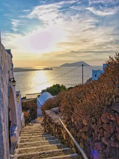 Stone steps leading down from Plaka village with a view of the bay of Milos and the island of Antimilos at sunset