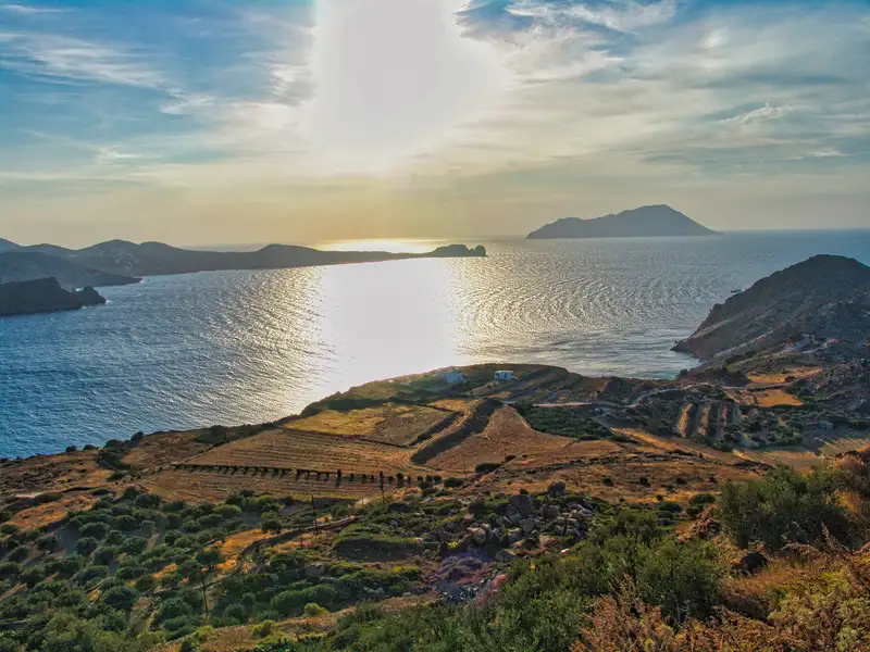 A panoramic view of the bay of Milos with terraced fields and the island of Antimilos in the distance at sunset