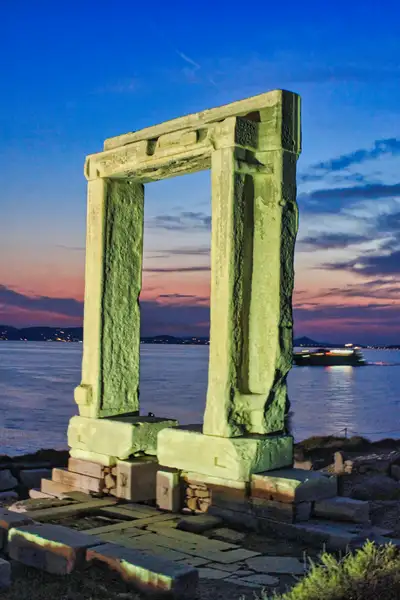 The Portara of Naxos lit at twilight with a ferry in the distance