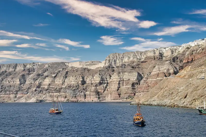 Wooden boats on a Santorini caldera tour in front of the layered volcanic cliffs