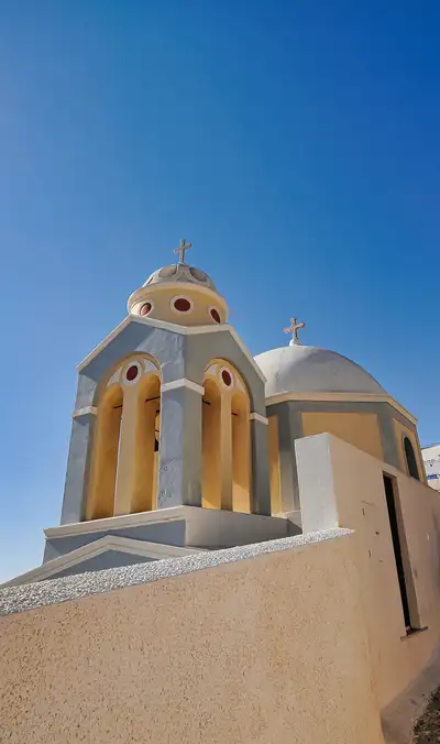 Ornate bell tower of a Santorini church with red detail and two crosses